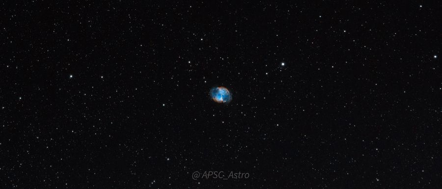 The small teal Dumbbell Nebula amid a wide star field
